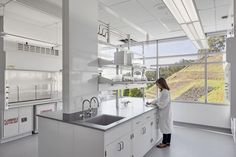 a woman in white lab coat standing next to a sink and window with large panoramic windows