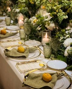 a long table is set with place settings and plates, silverware, lemons, and greenery