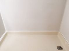 a white shower with a drain in the middle and a wall behind it that is painted white