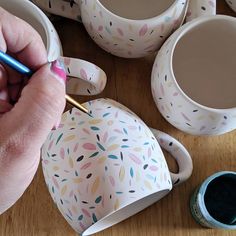 a person holding a pen in their left hand next to some cups and saucers