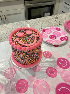 a birthday cake with sprinkles and smiley faces on the table next to plates