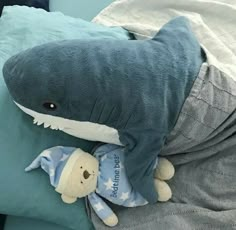 a stuffed shark laying on top of a bed next to a teddy bear