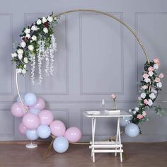 a wedding arch with balloons and flowers on the floor next to a small white table