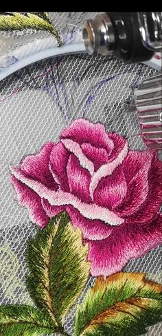 a close up of a pink rose on a piece of cloth with a needle and thread