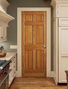 a wooden door in a kitchen next to a stove top oven and countertop with utensils on it