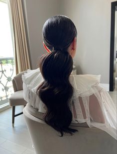 a woman with long black hair sitting in a chair looking out the window at something outside