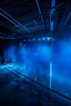 an empty room with blue light coming from the ceiling and fog in the air on the floor