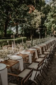 a long table is set up with white plates and place settings for an outdoor wedding