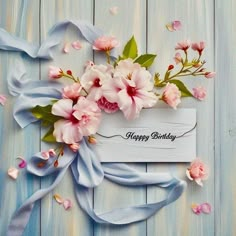 a happy birthday card with pink flowers and blue ribbon on a wooden background that says happy birthday