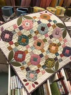 a quilted table top with many different colored fabrics on it and some other items in the background