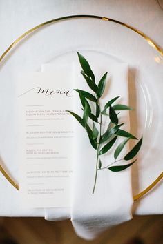 a place setting with white napkins and greenery on it, along with a gold rimmed plate