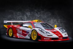 a red and white race car with yellow rims on it's tires is shown in front of a dark background