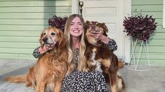 a woman sitting on the ground with two dogs in front of her and smiling at the camera