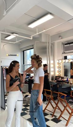 two women standing in front of a mirror with hair dryers on their heads and one holding a purse