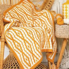 an orange and white crocheted blanket sitting on top of a wicker chair