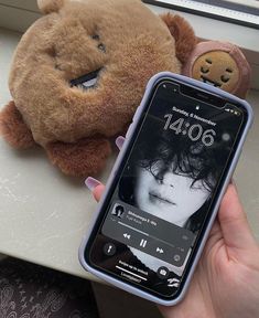 a person holding a cell phone next to a teddy bear