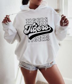 a woman wearing a white hoodie with the words tigers printed on it, standing in front of a mirror