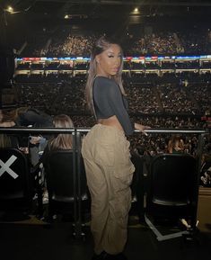 a woman standing in front of a crowd at a sporting event wearing khaki pants