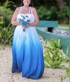 a woman in a blue and white dress is standing on the beach with her bouquet