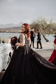 a woman in a black dress standing next to a white car and some other people