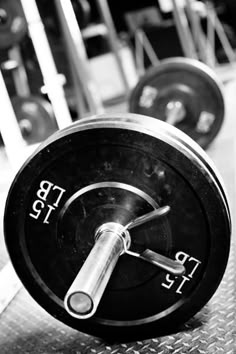 a black and white photo of a barbell in a gym with weight plates on the floor