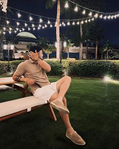 a man sitting on top of a wooden bench next to a lush green field at night