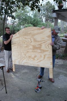 two men standing next to each other holding up a large wooden board on the ground