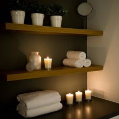 towels and candles are arranged on the shelves in this dimly lit bathroom, along with two white vases