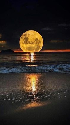 the full moon is shining brightly in the sky over the water and sand at the beach