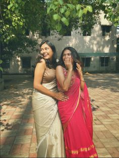 two women standing next to each other on a brick floored area with trees in the background