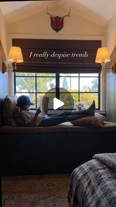 a man laying on top of a bed in a bedroom next to a window reading a book