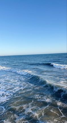 an ocean view with waves crashing on the shore and blue sky in the back ground