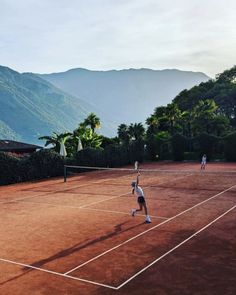 two people playing tennis on a clay court with mountains in the backgrouds