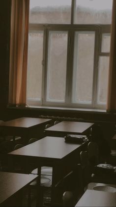 an empty classroom with tables and desks in front of a window that is partially open