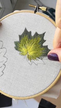 a woman's hand is holding a cross - stitch embroidery project with a green leaf on it