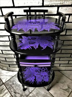 three tiered table with purple and black designs on the top, in front of a brick wall