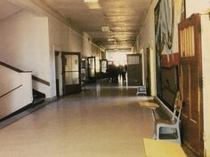 an empty hallway with several chairs and paintings on the wall, along with two people walking down the hall