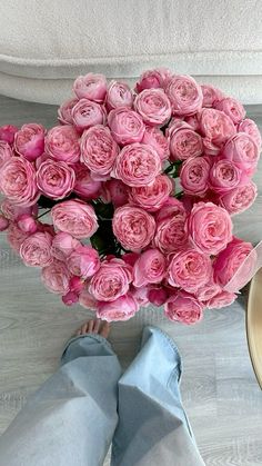 a bouquet of pink roses sitting on top of a wooden floor next to a person's feet