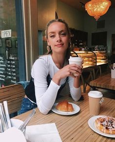 a woman sitting at a table holding a cup of coffee and eating doughnuts