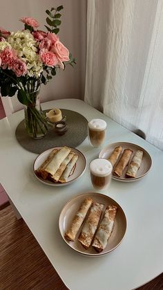 three plates with food on them sitting on a table next to a vase filled with flowers