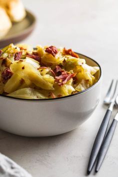 a white bowl filled with pasta and bacon on top of a table next to silverware