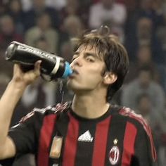 a man drinking from a bottle while standing in front of a soccer stadium full of people