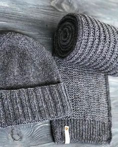 two gray knitted hats on top of a wooden table next to a roll of yarn