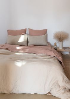 a bed with two pillows on top of it next to a table and vases