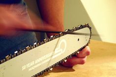 a man holding a chainsaw on top of a wooden table with the words 50 year anniversary written on it