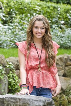 a beautiful young woman standing next to a rock