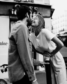 a man kissing a woman on the cheek as she stands next to a bike in front of a store