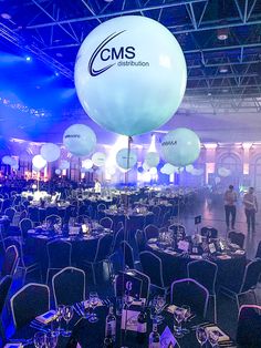 balloons and tables are set up in the middle of a room with people standing around