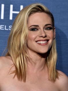 a woman with blonde hair smiling and wearing a strapless dress at the blue carpet event