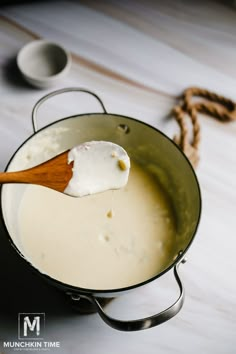 a wooden spoon in a pot filled with milk and sour cream on a white table